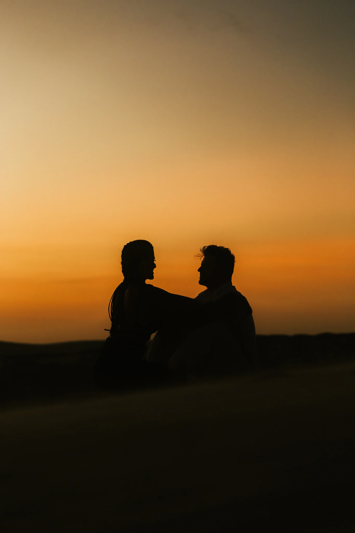 Fernanda e Rodrigo, da YUMI, em silhueta diante do pôr do sol em Taíba, Ceará